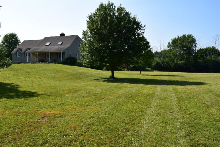 Sloping lawn with mowing stripes leading up to a gray country home - RN Land Management